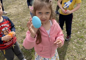 dziewczynka trzyma znalezione w ogrodzie kolorowe jajko